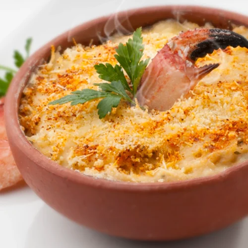 A steaming crab gratin in a clay pot, garnished with parsley and breadcrumbs, with crab claws on the side.