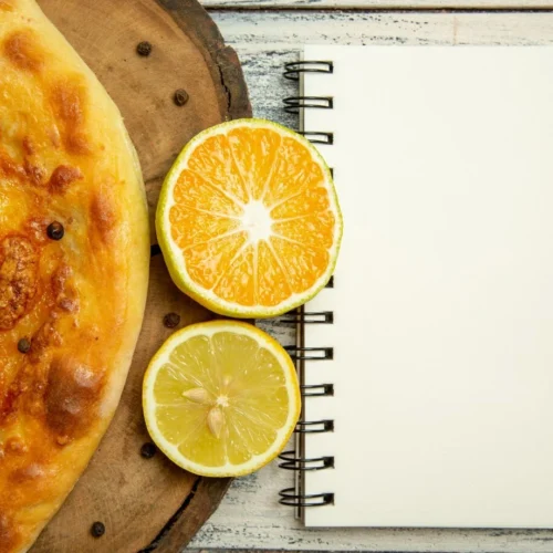 Orange Zest Low Card Dessert : A fresh-baked khachapuri with a sunny-side-up egg, next to halved orange and lemon slices and a blank notepad on a rustic wooden surface.