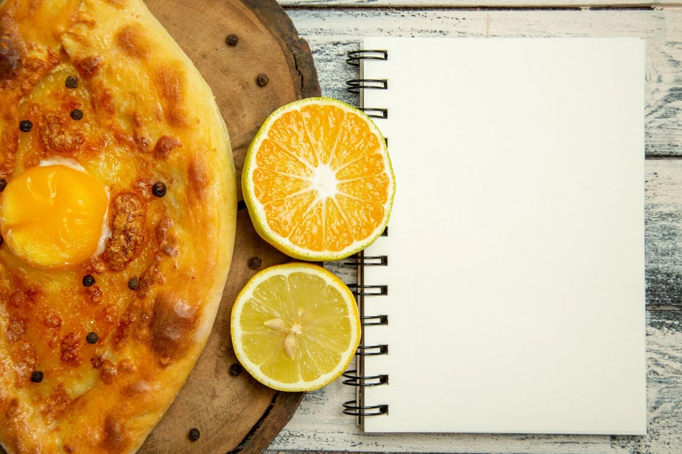 Orange Zest Low Card Dessert : A fresh-baked khachapuri with a sunny-side-up egg, next to halved orange and lemon slices and a blank notepad on a rustic wooden surface.