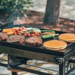 A Blackstone griddle sizzling with various foods, including steaks, vegetables, and pancakes, showcasing its versatility.