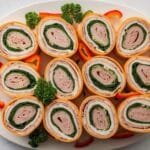 A platter of freshly prepared Swiss turkey rolls arranged neatly with cream cheese, Swiss cheese, and fresh vegetables inside.