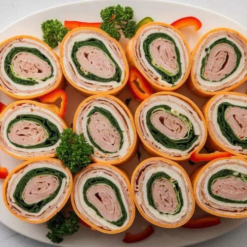 A platter of freshly prepared Swiss turkey rolls arranged neatly with cream cheese, Swiss cheese, and fresh vegetables inside.